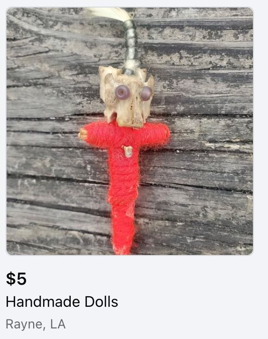 Picture of a red voodoo doll. Purple beads are glued onto an animal bone to make a face. 