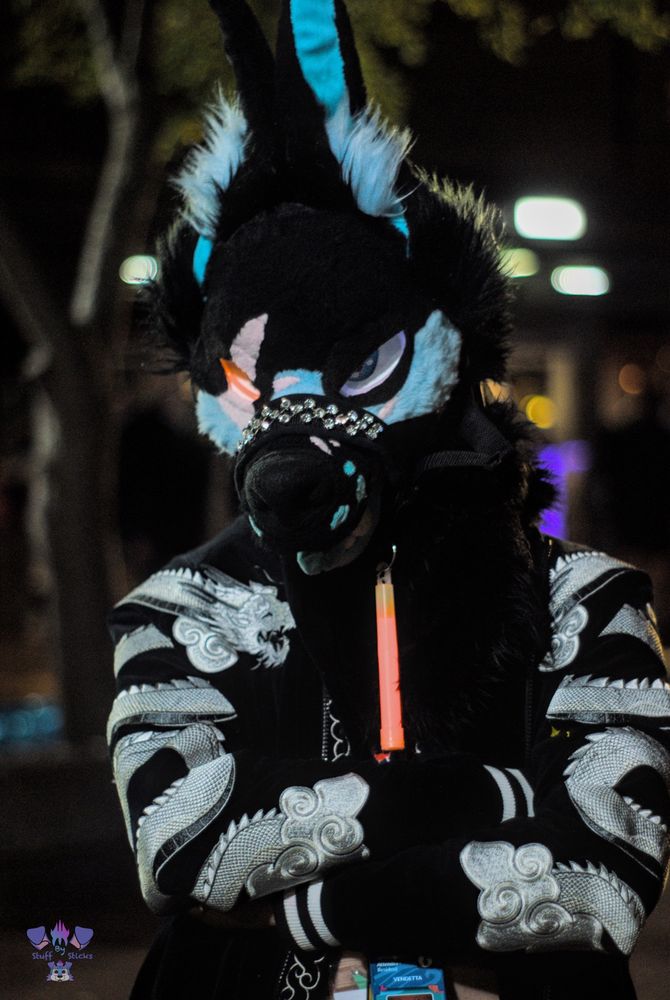 Mid shot of the fursuiter Vendetta with their arms crossed as their eyes glow 