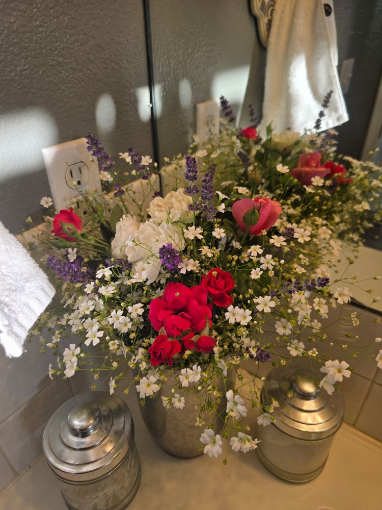 A bouquet of roses, lavender, and baby's breath graces the corner of a bathroom countertop next to a mirror.