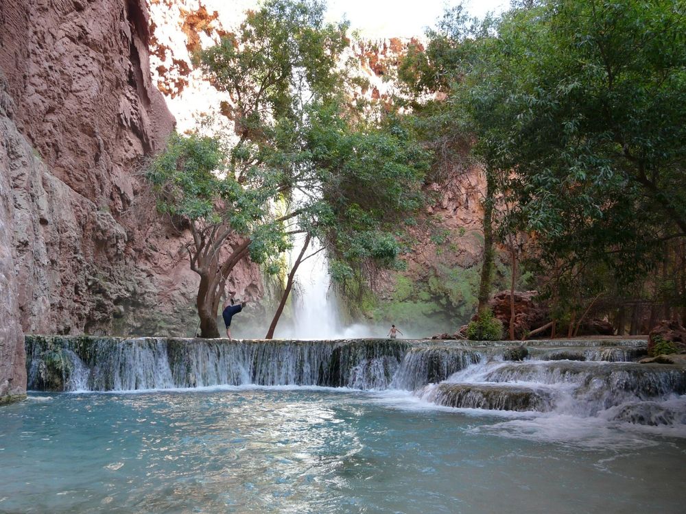 Me swinging off a rope from a tree into a pool of water before a ~2 meter travertine waterfall. In the distant background is another waterfall a couple hundred feet tall.
