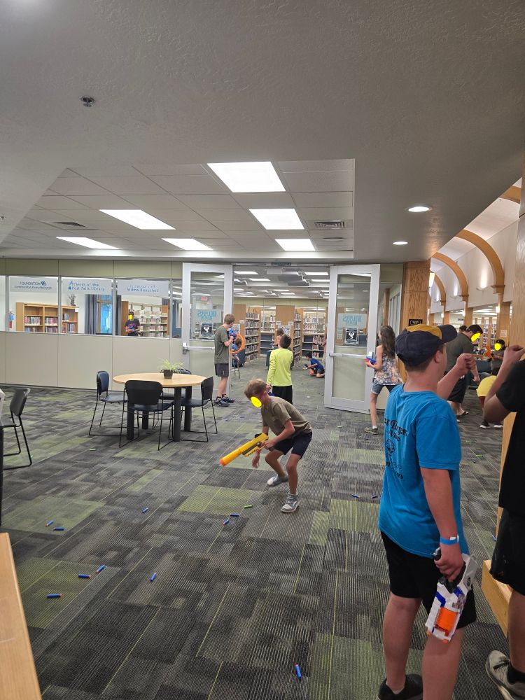 A bunch of kids scrambling around a library with Nerf guns. The floor is covered in bullets.