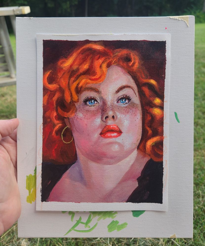 Am acrylic painting of a beautiful red haired woman with freckles and blue eyes. She is plus sized and has one gold earing and a black sweater. Some greenery is seen around