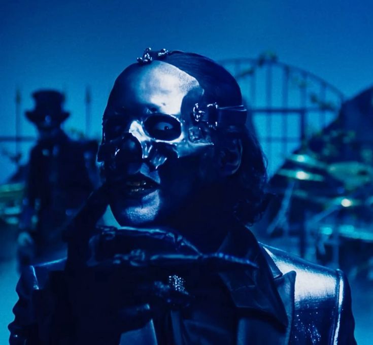 Cena do clipe de Lachryma, da banda Ghost, com um close no vocalista Papa V Perpetua. Ele tem os cabelos na altura do queixo, usa uma máscara brilhante e um dos olhos tem uma lente branca.