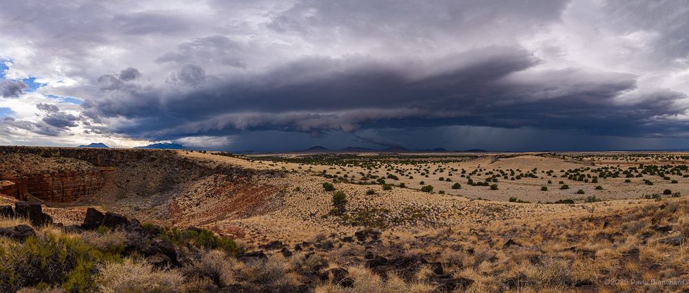 A band of thunderstorms with a shelf cloud is visible in the distance. In the foreground is a large sinkhole on the left and grasslands elsewhere.