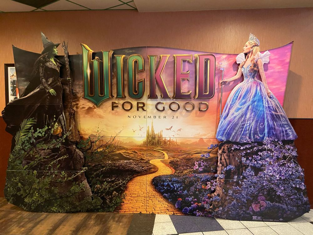 A large display for Wicked: For Hood shoeing Elphaba and Glinda on opposite sides of the yellow brick road. The Emerald City can be seen in the background.