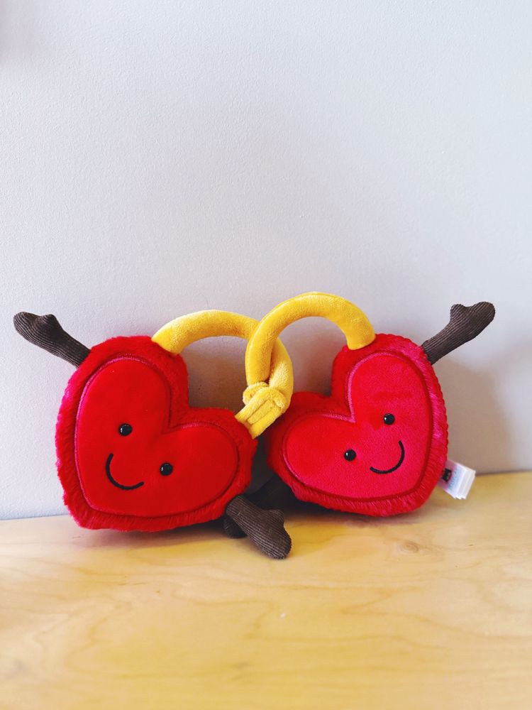 The Jellycat Love Locks. Two cuddle red heart-shaped locks, linked together with yellow rings that are velcroed. They both have smiling faces and little arms. 