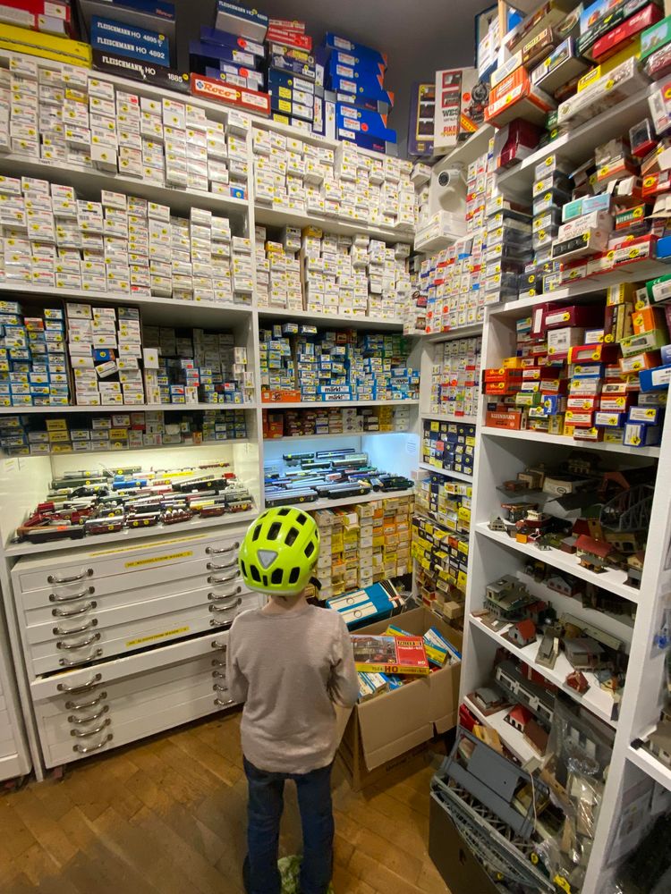 Kind mit neon gelbem fahrradhelm steht mit dem Rücken zur Kamera vor 3 Meter hohen Regalen voller märklin modeleisenbahnen in Kartons und unverpackt 