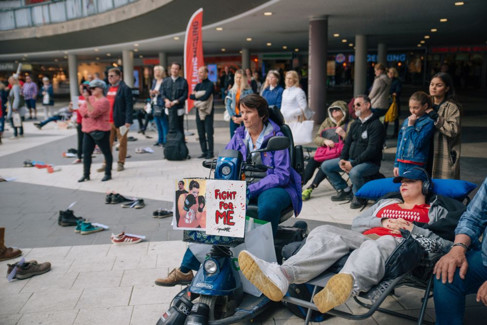 Foto av flera personer som står på Sergels torg. På torget flera par tomma skor. En person med en skylt det står "Fight for ME" på. Foto: Linnea Sandberg