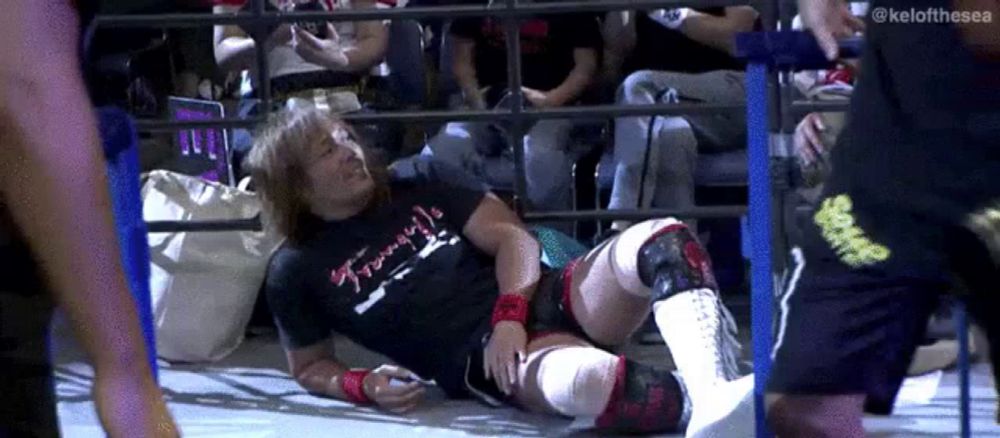 a wrestler is laying on the floor in a ring while a crowd watches .