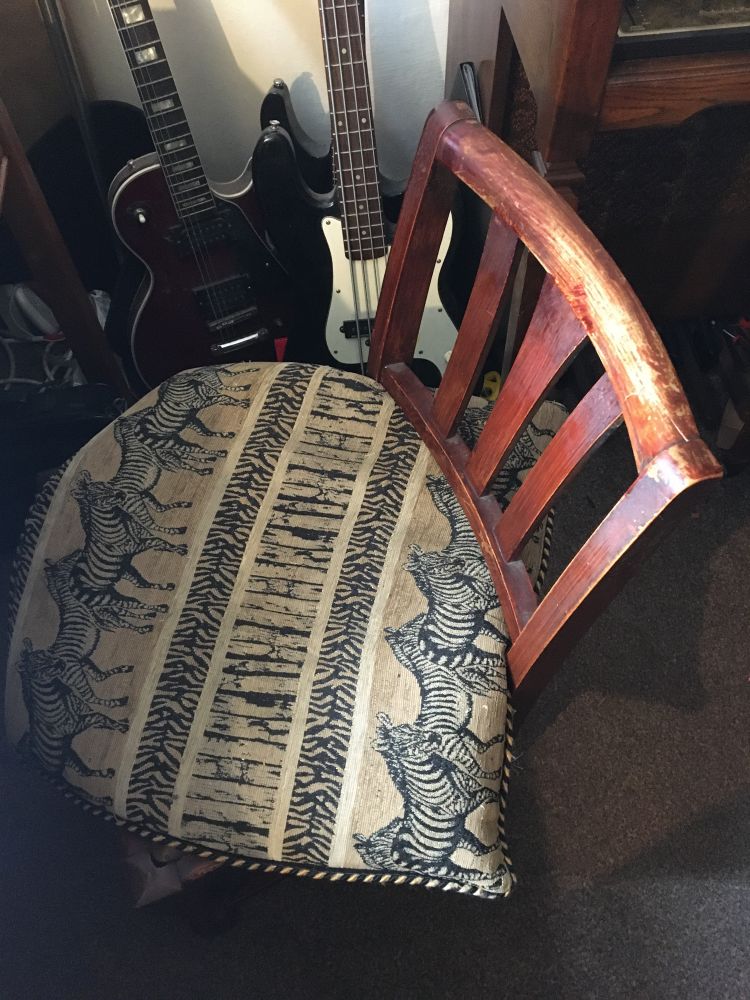 An old wooden chair with a cushion on it. There are some old dusty guitars in the background.