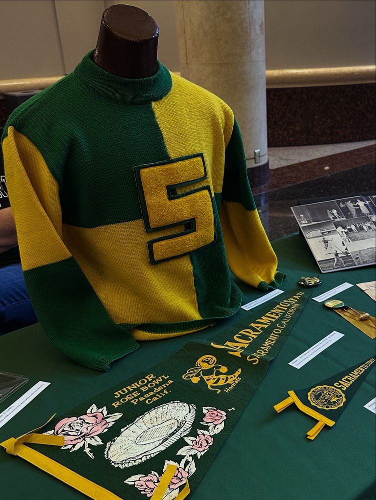 A display of green and yellow Sacramento State memorabilia, including pennants and a cheer sweater. 