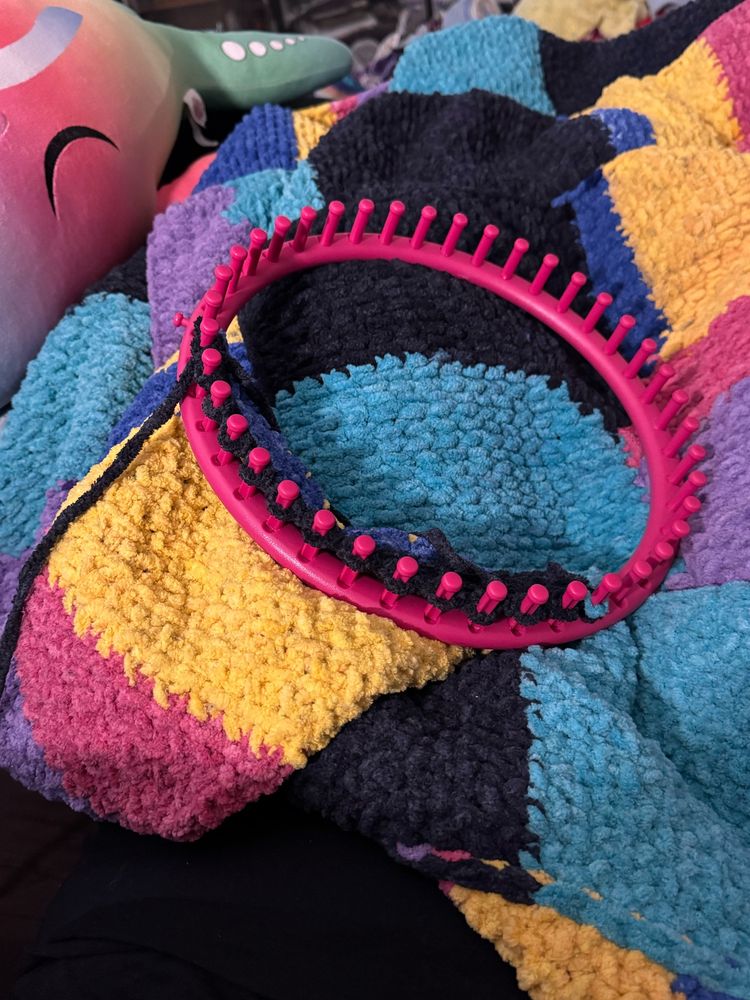 Photo of my current WIP blanket on top of me, featuring my loom in the center of the frame to show that this is still being worked on.