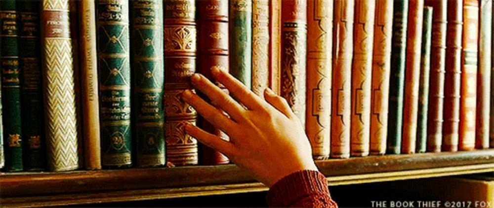 a person 's hand is reaching for a book on a bookshelf with the book thief written on the bottom right