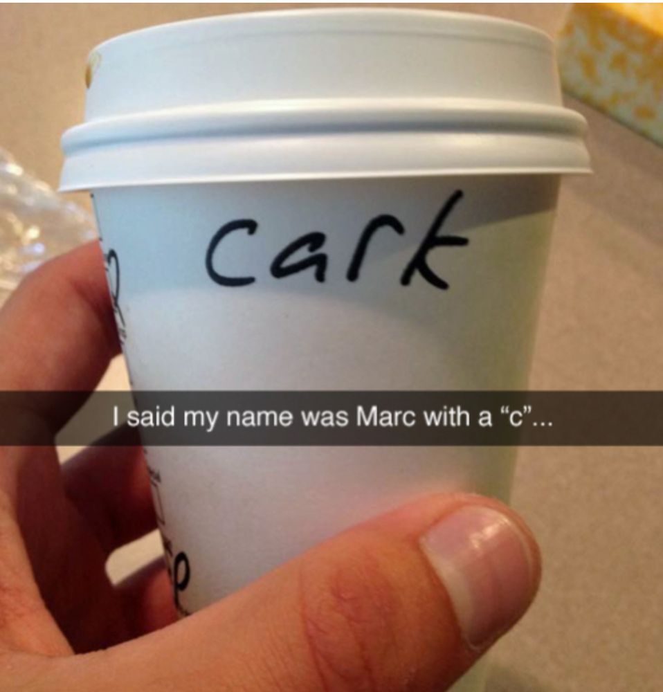 A photo of a hand holding a takeout coffee cup with cark written on it in permanent marker. A caption across the photo says: I said my name was Marc with a "c"...