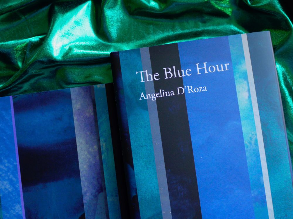 The back and front jacket of 'The Blue Hour' by Angelina D'Roza, white text against vertical bands of bluish colour, set against a background of green silken folds.