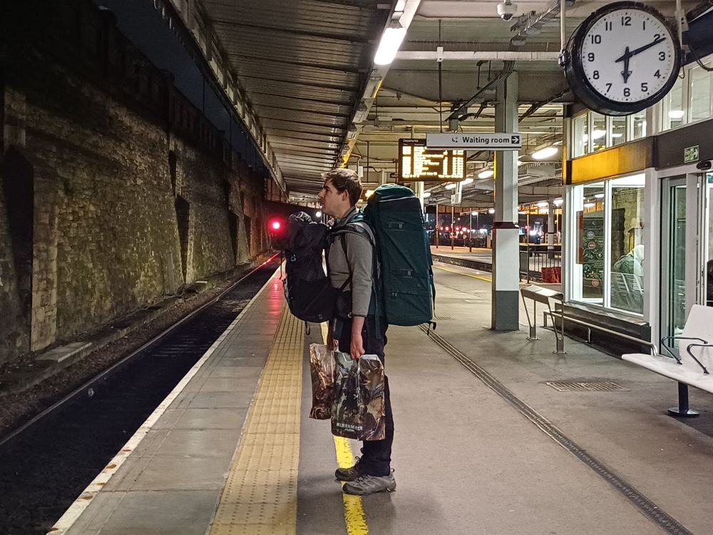 The editor of Longbarrow Press, en route to the Small Publishers Fair in Holborn, London, with stock and accessories in two rucksacks and two carrier bags. Sheffield Midland Station, 6.11am, 27 October 2023. Photograph by Emma Bolland.