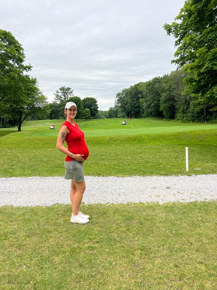 I am posing next to a golf green holding my 7 months pregnant belly.
