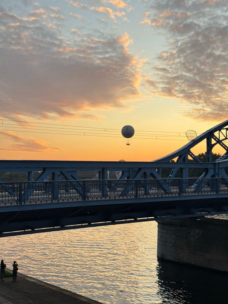 Photograph: a bridge over river Wisła, sunburnt sunset in the background with a balloon rising above the bridge