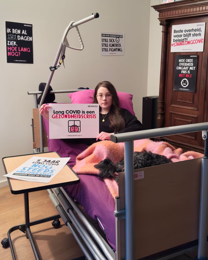 Guus is een vrouw met lang bruin haar en een bril. Ze ligt in een hooglaagbed met een paars laken en een roze-oranje deken in een woonkamer. Een klein zwart hondje rust naast haar op het bed. Ze heeft een serieuze blik en houdt een protestbord vast met de tekst: "Long COVID is een GEZONDHEIDSCRISIS". In de kamer hangen meerdere posters en borden aan de muren, geschreven in het Nederlands, die pleiten voor bewustwording en sterker beleid voor Long COVID-patiënten. Op een van de posters staat: "Ik ben al 1521 dagen ziek. Hoe lang nog?". Op een ander bord op het nachtkastje staat: "5 jaar Long COVID. Nog steeds geen beleid". Op de achtergrond staat een houten kast.