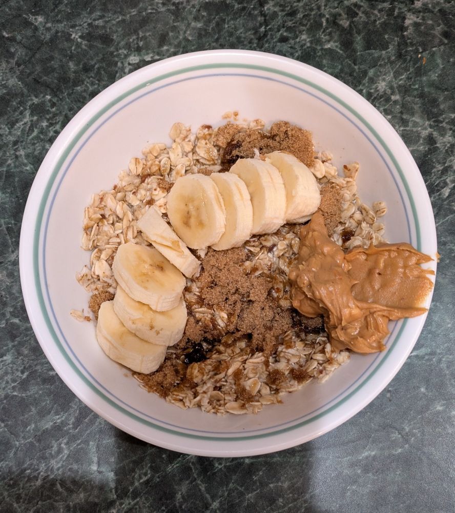 A bowl of instant oatmeal with banana slices and a dollop of peanut butter on the side. The brown sugar is starting to get saturated. 