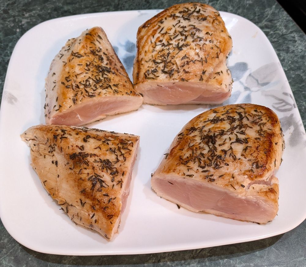 2 large chicken breasts on a plate, each cut in half. The top and bottom are well browned and is seasoned with coarse salt, thyme, and parsley. 

The center of the chicken can clearly be seen to be mostly pink and uncooked 