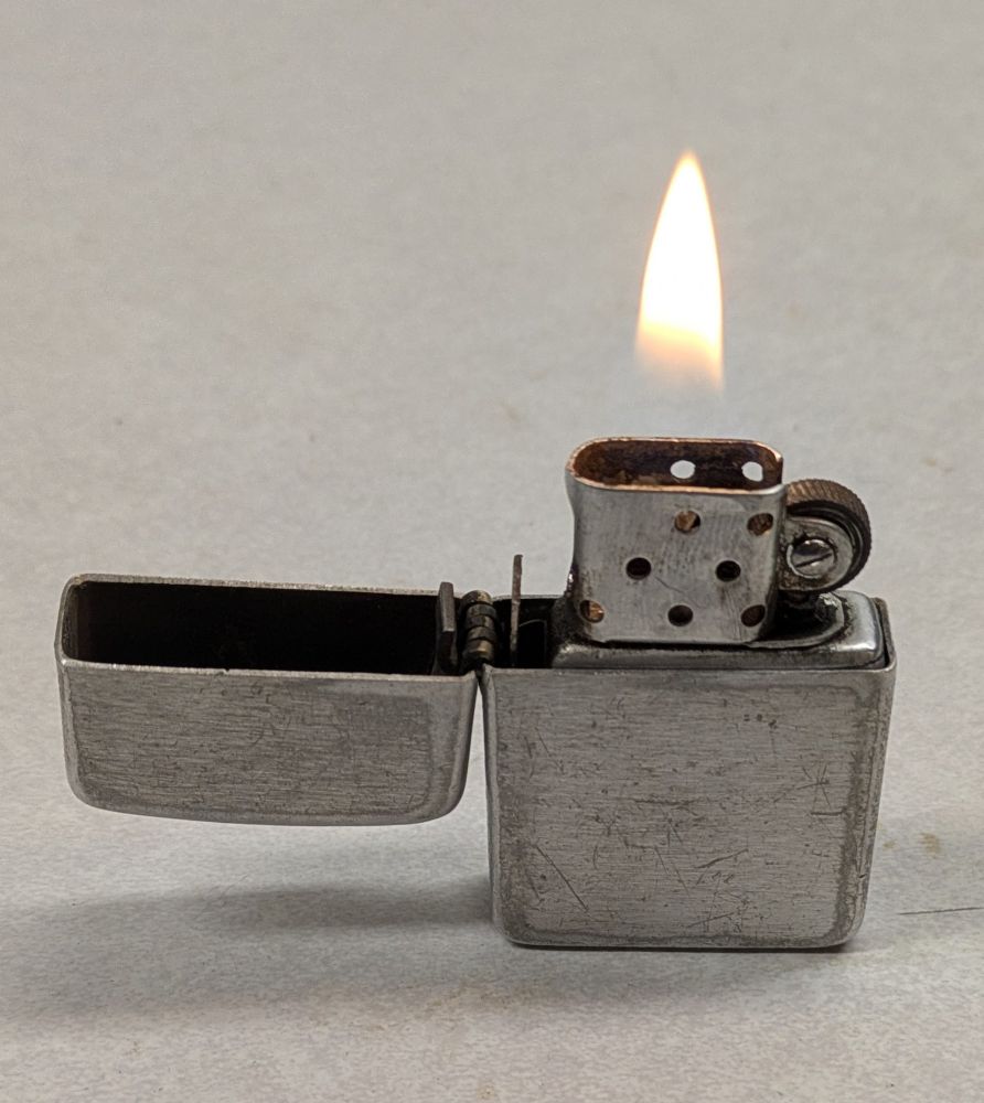 A Zippo lighter, sitting open on a workbench with a nice flame. 