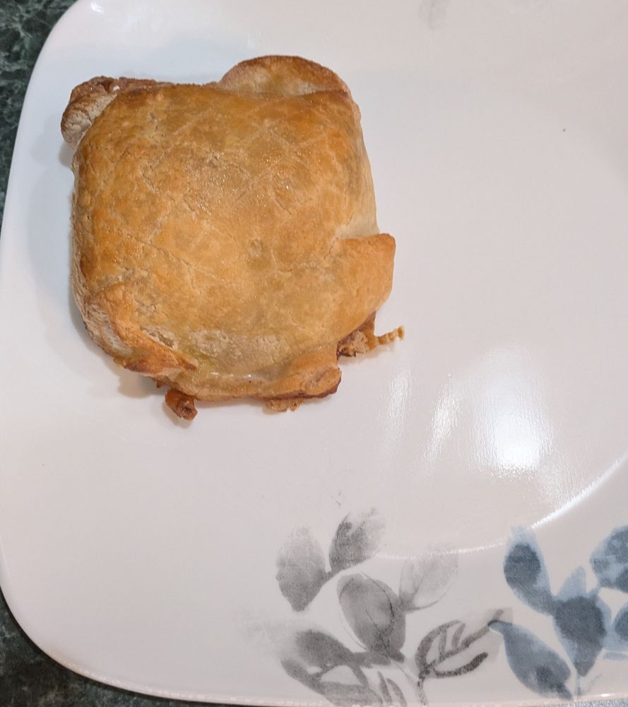 Finished Chicken Wellington on a plate. The puff pastry is golden brown, the scoring isn't clearly visible in this lighting and view. 

The wrap and fold aren't as tight as you'd see with regular (not gluten free) pastry. 