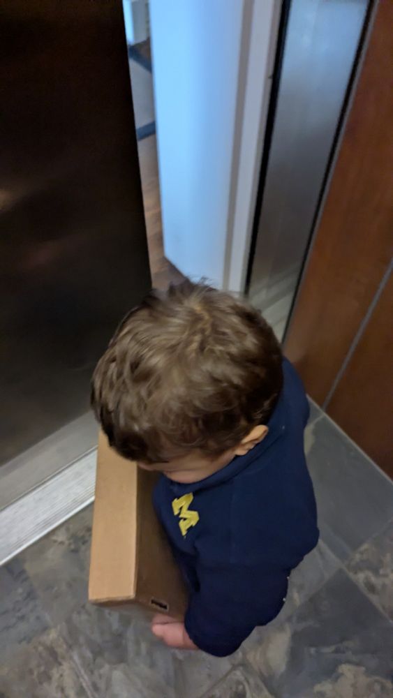 A toddler holding a package containing the mgoblog book "Victors"