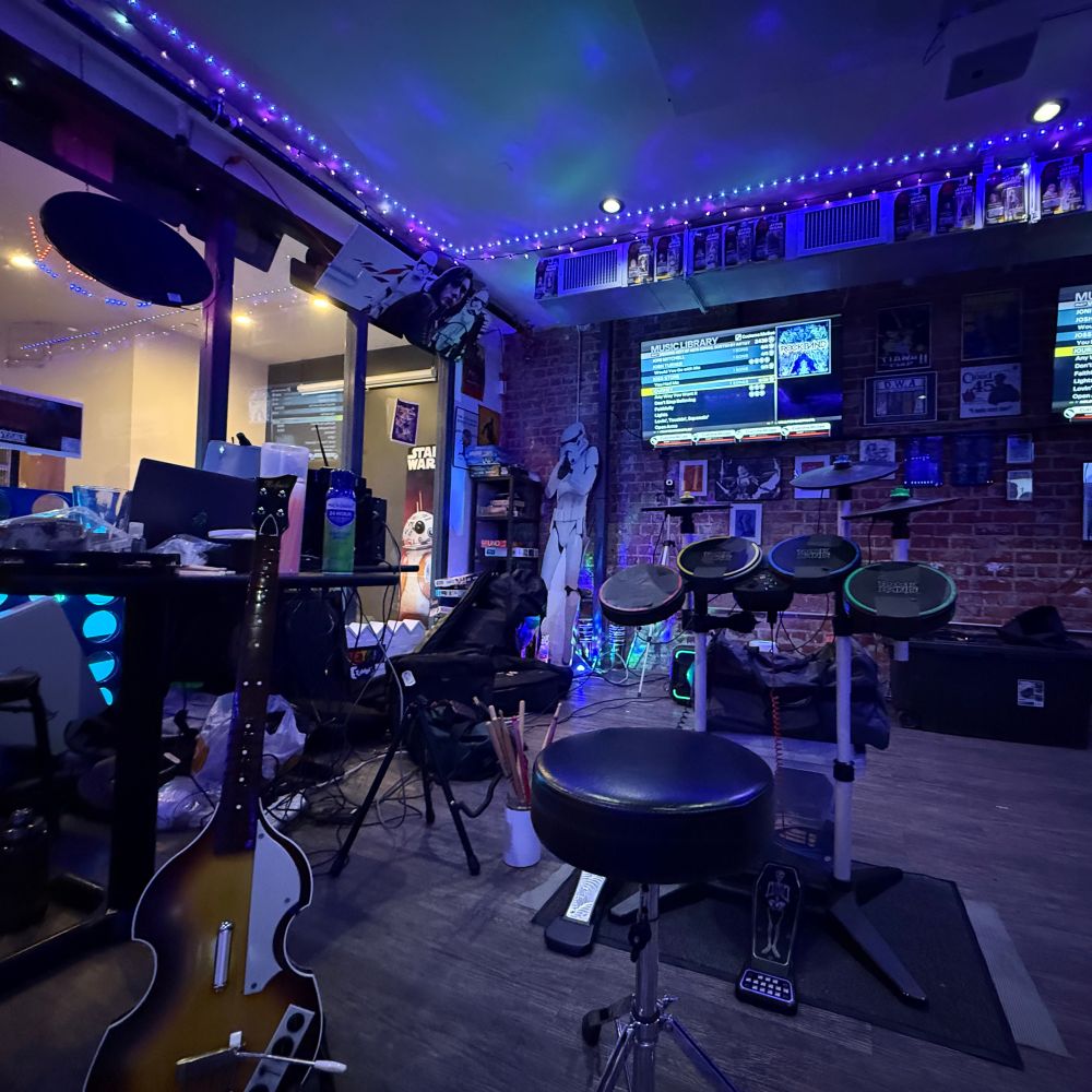 A bar with a set up for Rock Band visible on two TVs, with a rock band drum set and a plastic bass from the Beatles Rock Band. 
