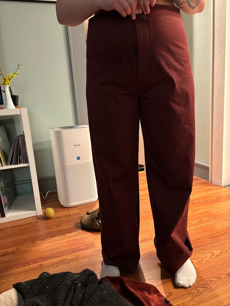 A woman wearing a pair of oxblood colored trousers, viewed from the front to show the fit issues.
