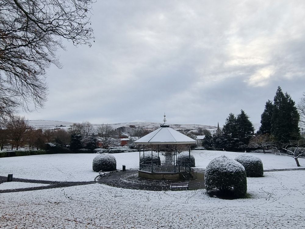 Victorian park bandstand in the snow with hills and sky in the background