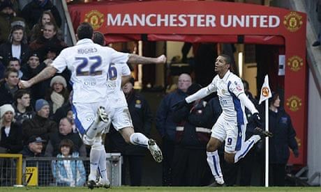 This photo shows a moment during a football match with a player celebrating in front of the corner flag. The background features the “Manchester United” tunnel at Old Trafford, suggesting this game took place at Manchester United’s home ground. It depicts a significant moment, possibly from a cup or league game, given the intensity and iconic setting.