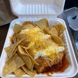 A wet burrito swimming in cheese sour cream and chips.