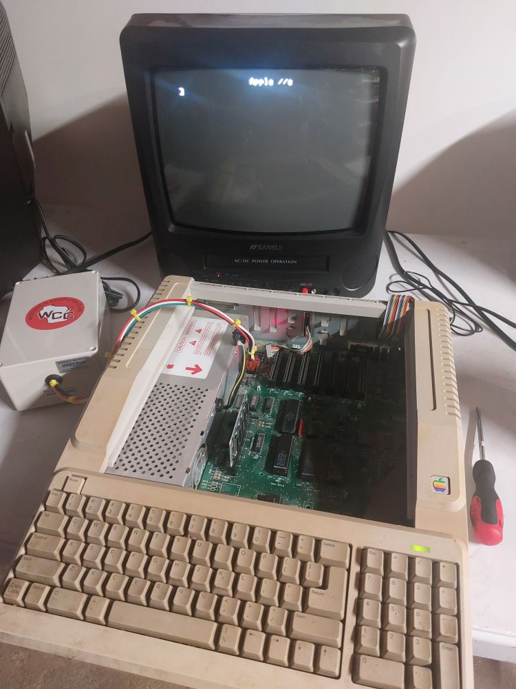 An Apple 2e Platinum computer powered up on a table. The monitor displays the 