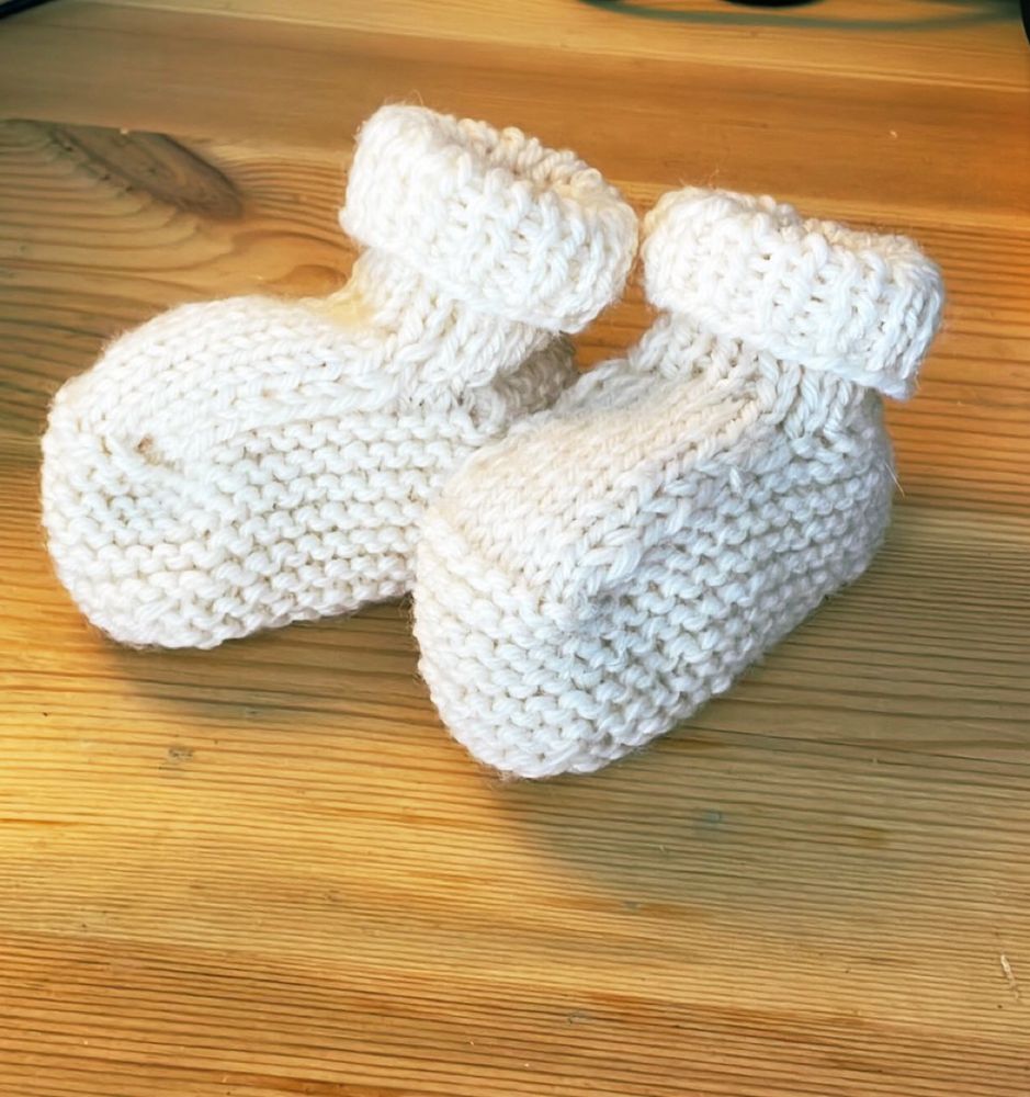 A pair of white hand-knitted booties to fit a newborn. 