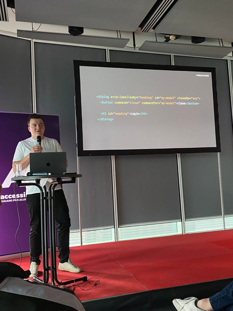 Manuel on stage presenting an HTML code snippet.