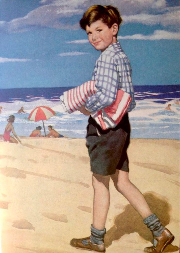 A boy walks along the beach, wearing a long sleeved shirt and shorts and carrying a towel under his arm. He is wearing socks and Start-rite sandals. and is looking straight at the viewer.
