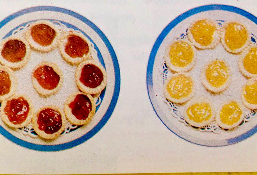Photograph showing two plates of home-made jam tarts. The ones on the left have been made with strawberry or raspberry jam and the ones on the right are lemon curd