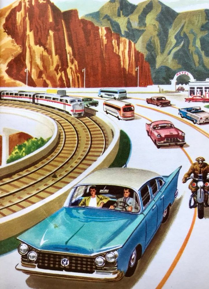 A curved highway running along besides the rail track, cuts through a pass in Western America, edged with rugged red rocky outcrops