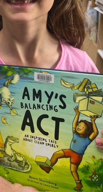 Young girl borrowing Amy's Balancing Act - a book about Clean Energy from her local library