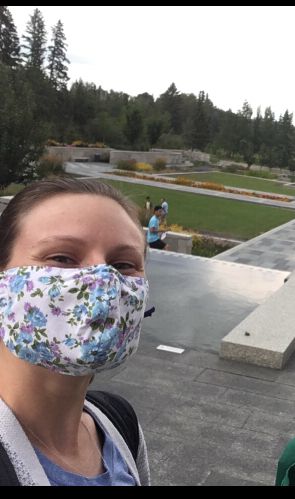 Selfie of a white woman wearing a floral cloth mask in an outdoor botanic garden. 