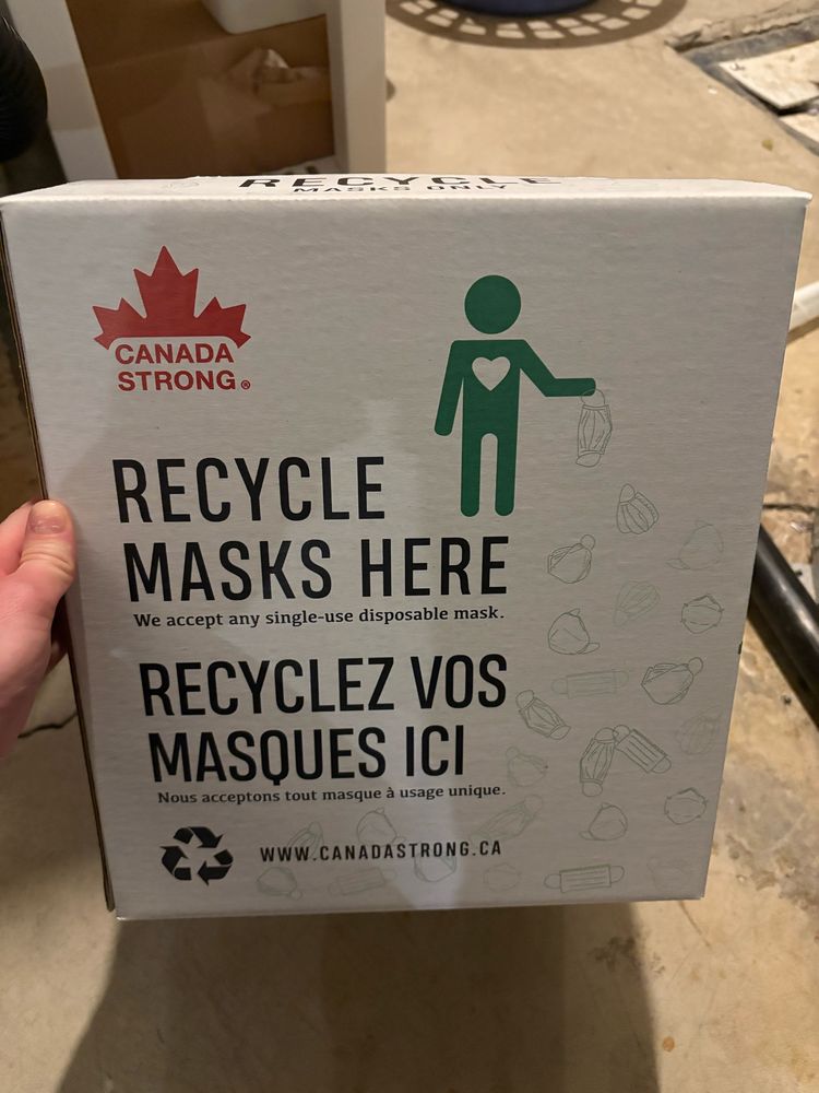 Image of a white box from Canada Strong (red logo with maple leaf over wording), that reads “Recycle Masks Here. We accept any single-use disposable mask.” 
“Recyclez vos masques ici. Nous acceptons tout masque à usage unique.” 
www.canadastrong.ca
The box also depicts a green stick figure of a person with a white heart, holding a used surgical mask. Different types of disposable masks are depicted on the box, including respirators. 