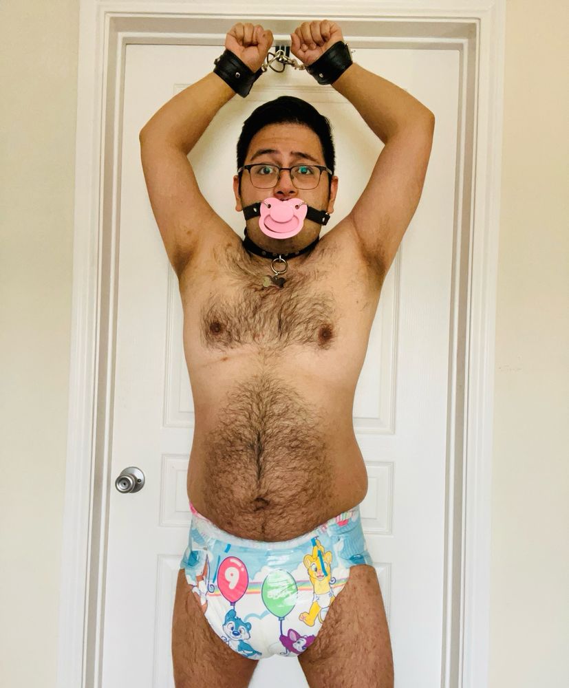 My punishment: I’m handcuffed with my cuffs connected to a strap that’s locked behind the door. The door is locked with my hands above my head so I can’t escape. Of course I’m wearing nothing but my huge diaper and pacifier gag. 