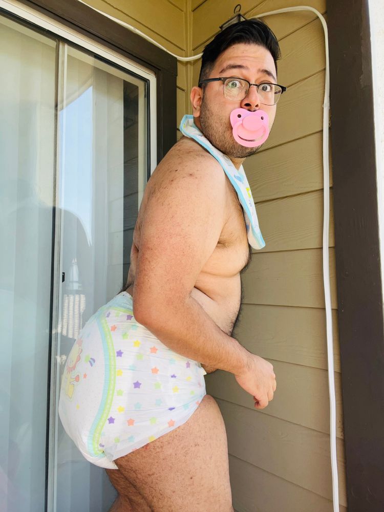 Locked out on the patio, I have a surprised look on my face as if I’ve just been walked in on in a very humiliating situation. I’m wearing nothing except a thick little kings diaper, bib, and pacifier. 