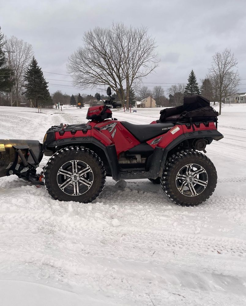 Photo of a red Polaris Sportsman 850 ATV with a 60” snow plow, sitting in the snow, ready to get to work
