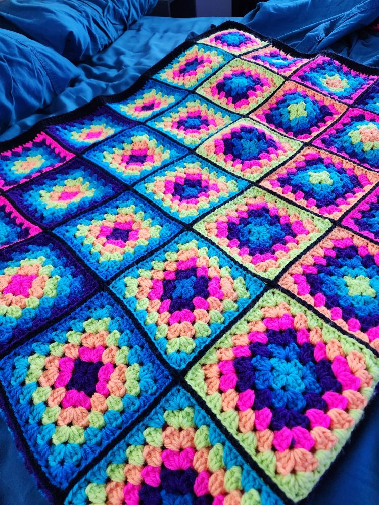 A folded granny square crochet blanket made of neon rainbow colors