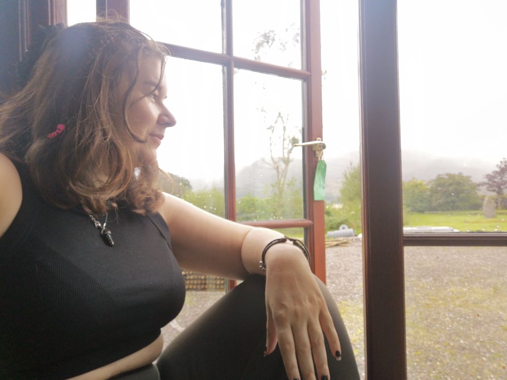Muso sat on the windowledge by a tall opened window, overlooking the Scotting mountainscapes whilst the mist rolls in. 