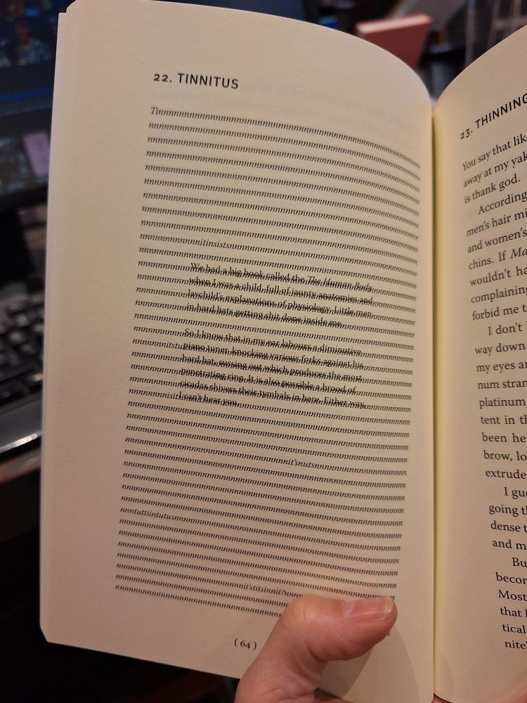 A hand holds a book open. At the top of the left page is the title '22. Tinnitus'. The rest of the page is unreadable. 