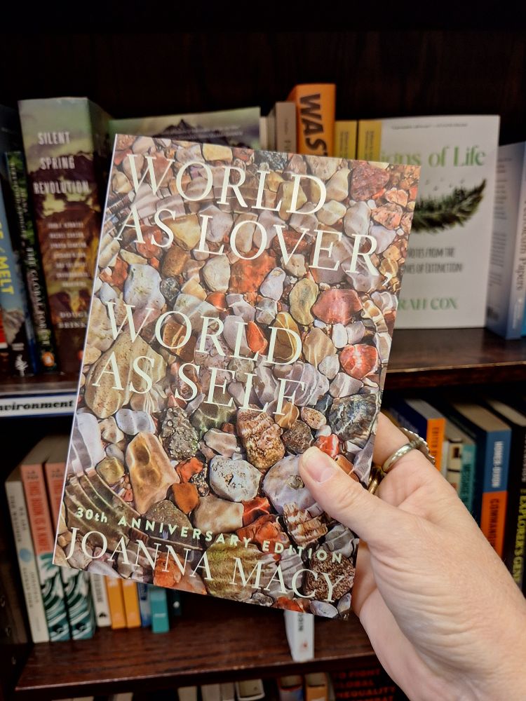 A hand holds up a copy of 'World as Lover, World as Self', by Joanna Macy.
