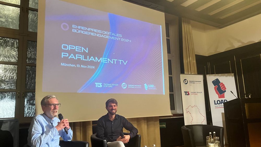 Foto der anschließenden Fragerunde mit Präsentation "Open Parliament TV" im Hintergrund
